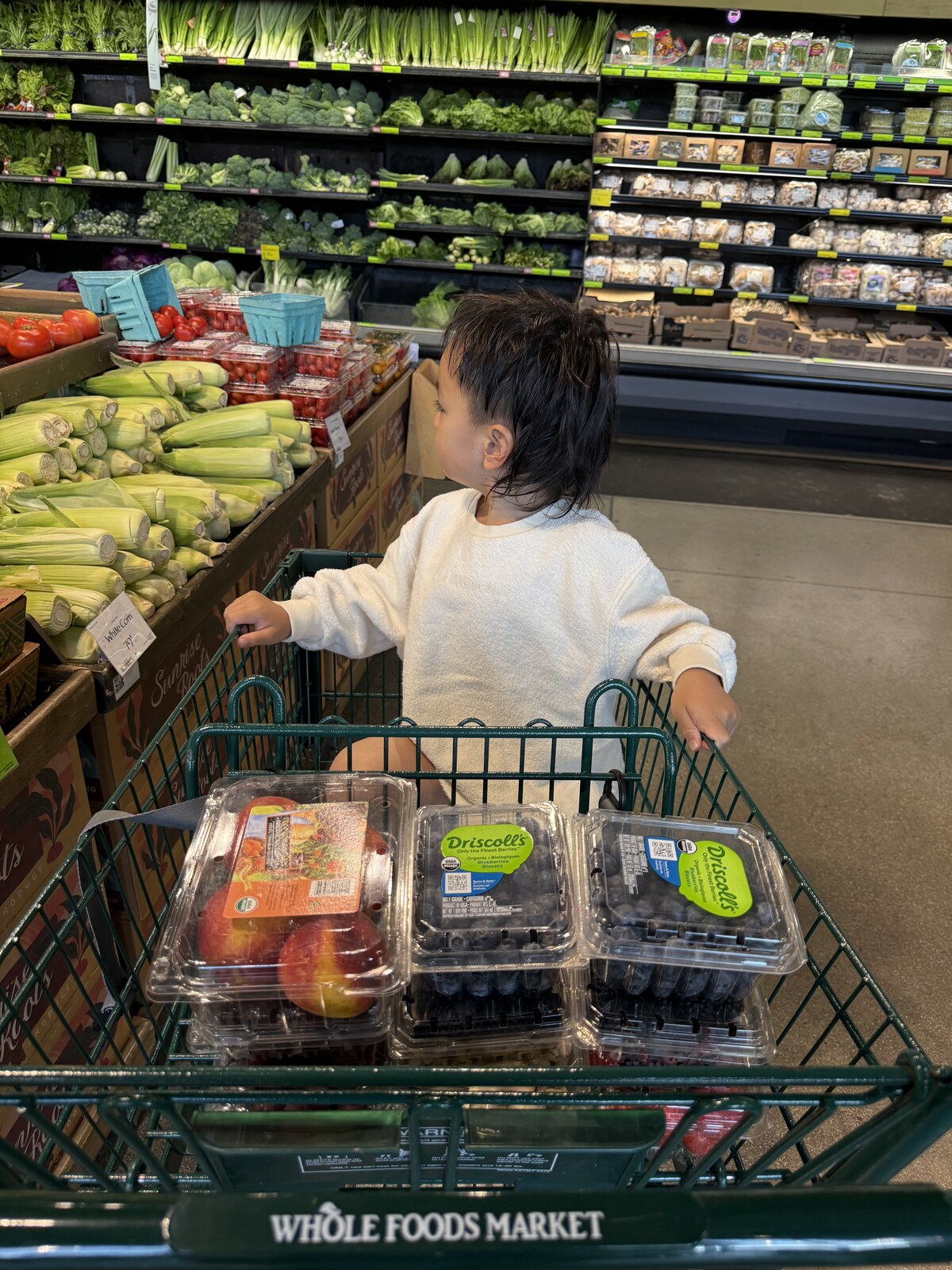 Jichang sitting in a Whole Foods cart with peaches, blueberries, strawberries, and blackberries