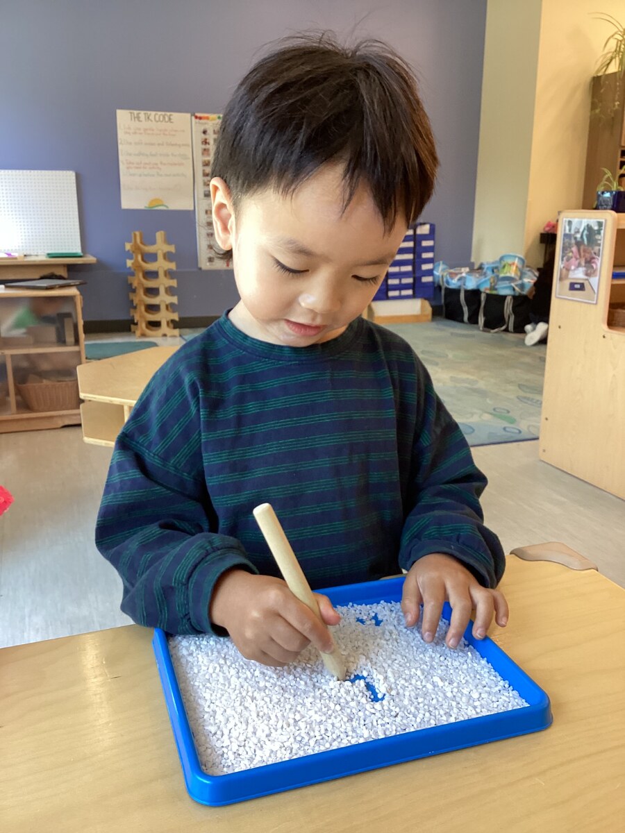 Jichang writing numbers in a sand tray at school