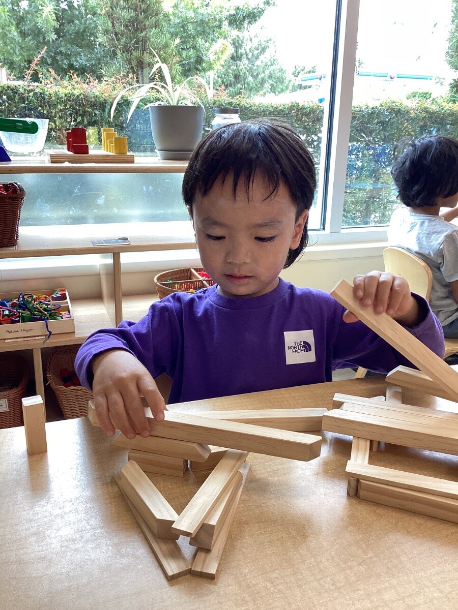 Jichang building a home shape with wooden blocks during a classroom activity