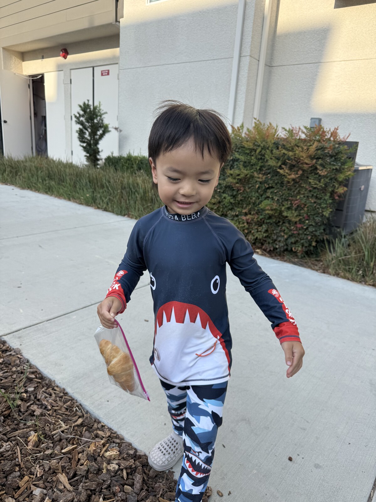 Jichang walking to the car in a shark swim suit while holding a croissant