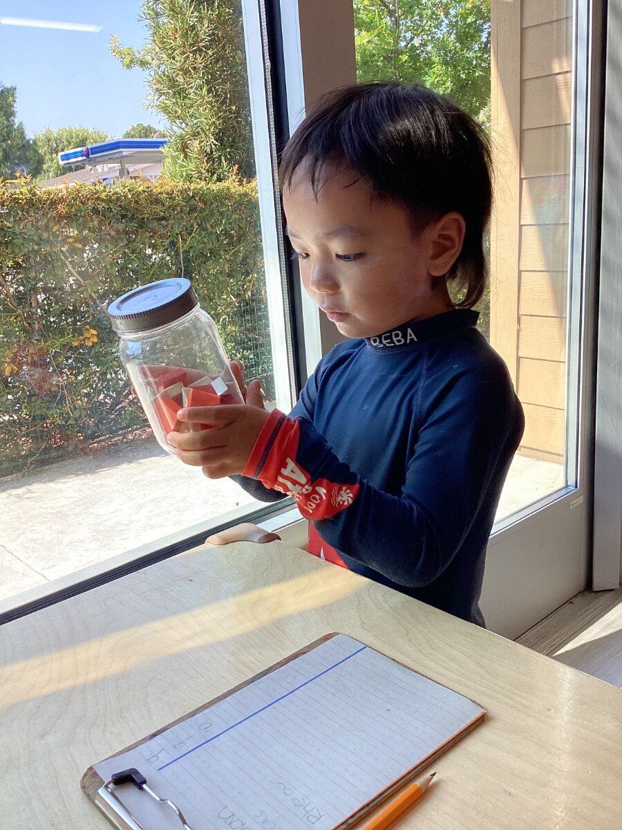 Jichang holding a clear jar filled with pattern blocks during an estimation activity